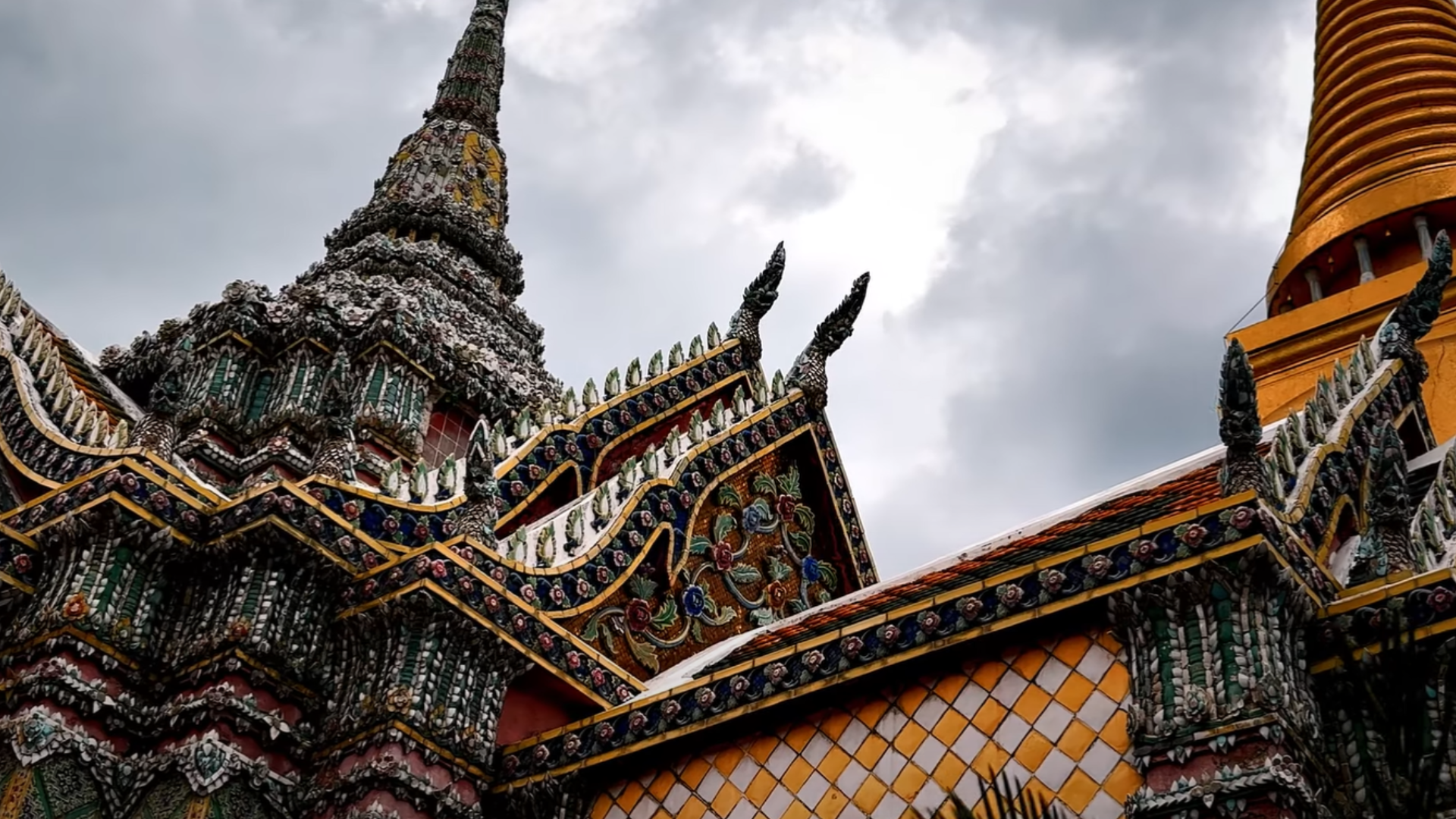 The colorful and ornate rooftops of Wat Phra Kaew temple in Bangkok, Thailand, with a tall central spire adorned with golden decorations.