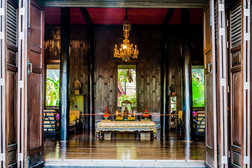 Ornate interior of a traditional Thai house with teakwood walls, antique furniture, and a crystal chandelier.