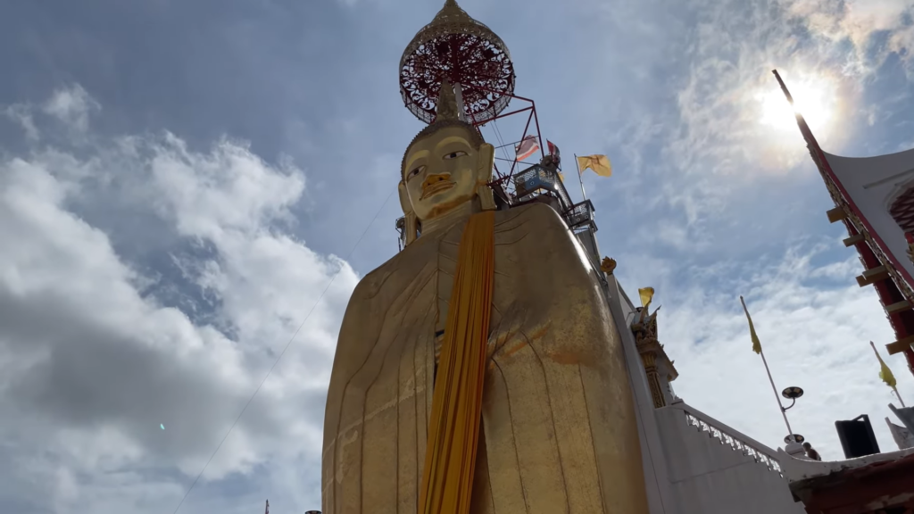 The giant golden standing Buddha statue at Wat Intharawihan temple in Bangkok, Thailand, with flags and scaffolding in the foreground.