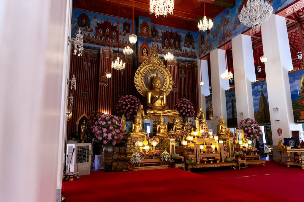 Wat Chana Songkram, a Bangkok temple, features a gold Buddha statue as its centerpiece. The interior is adorned with flowers and hanging chandeliers.
